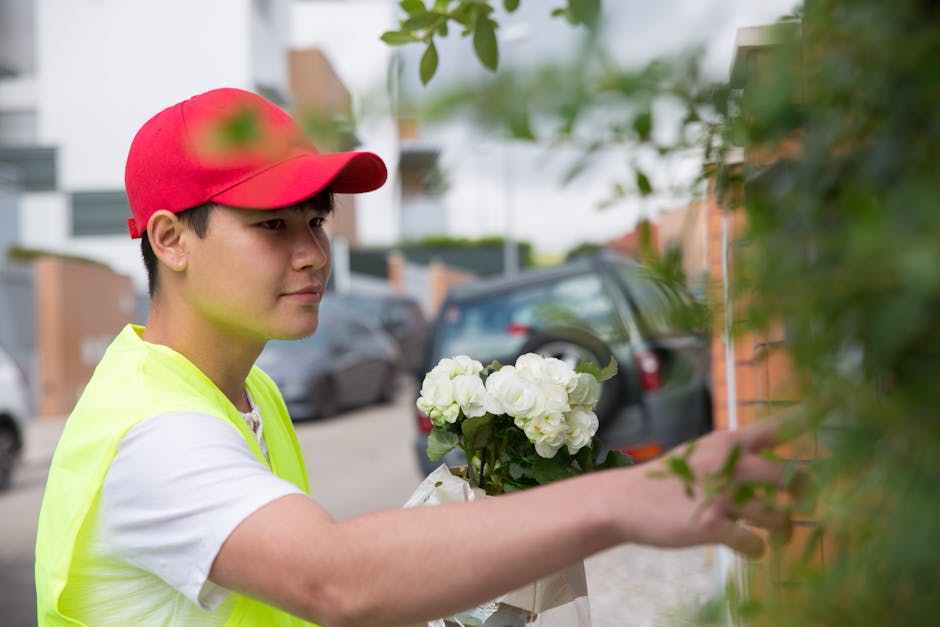 A young male florist wearing a red cap and a bright yellow high-visibility vest is seen delivering a floral gift. He is holding a bouquet of white hydrangeas with fresh, vibrant petals and green stems