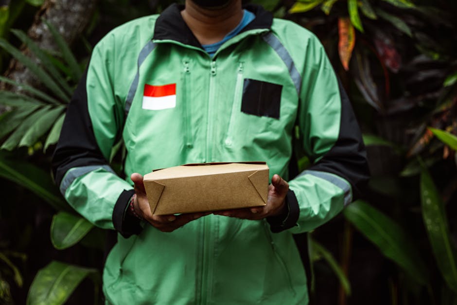 A delivery person wearing a bright green jacket with black sleeves, featuring a red and white flag patch on the left side and a black rectangular patch on the right side, is holding a rectangular card