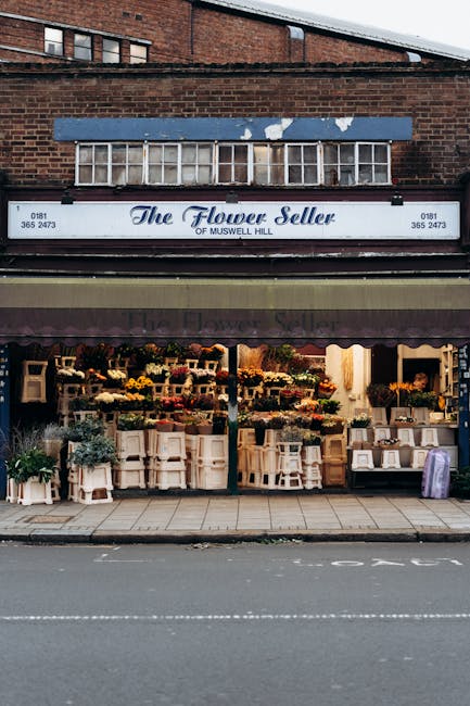 The exterior of 'The Flower Seller' shop in Muswell Hill, featuring a large sign with the store's name and contact information. The shop's window displays an array of fresh floral arrangements and bou